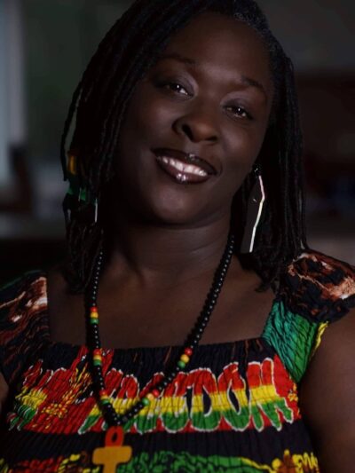 A photo of Brittany Martin. She is wearing a green, red, yellow, and black top and is smiling at the camera.