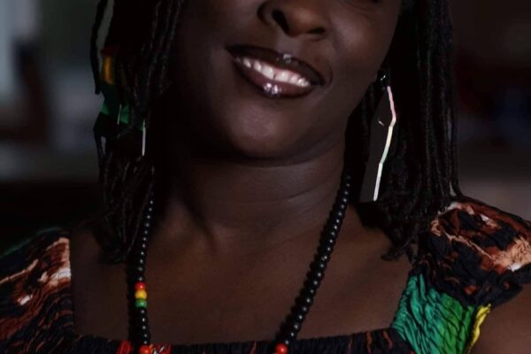 A photo of Brittany Martin. She is wearing a green, red, yellow, and black top and is smiling at the camera.