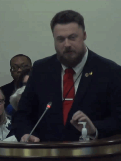 ACLU-SC Advocacy Strategist Matthew Butler addresses a subcommittee. He is wearing a suit and red tie and is standing behind a lectern with a microphone.