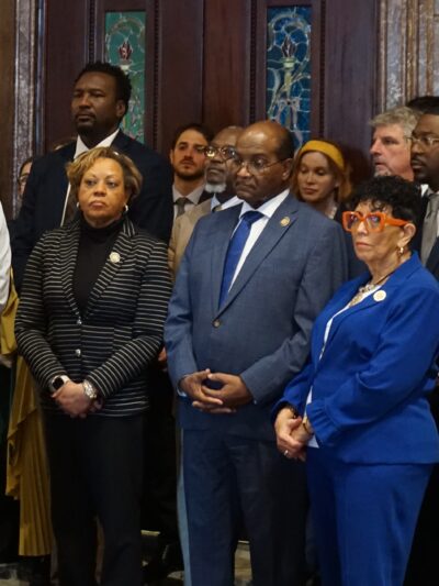A crowd of people in businesswear stands behind a speaker at a lectern in the South Carolina State House lobby