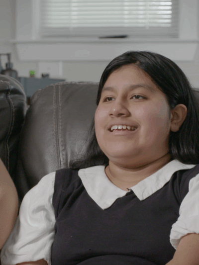 Skyler, a 13-year-old boy, smiles while talking. He is seated on a brown leather couch beside his mother.