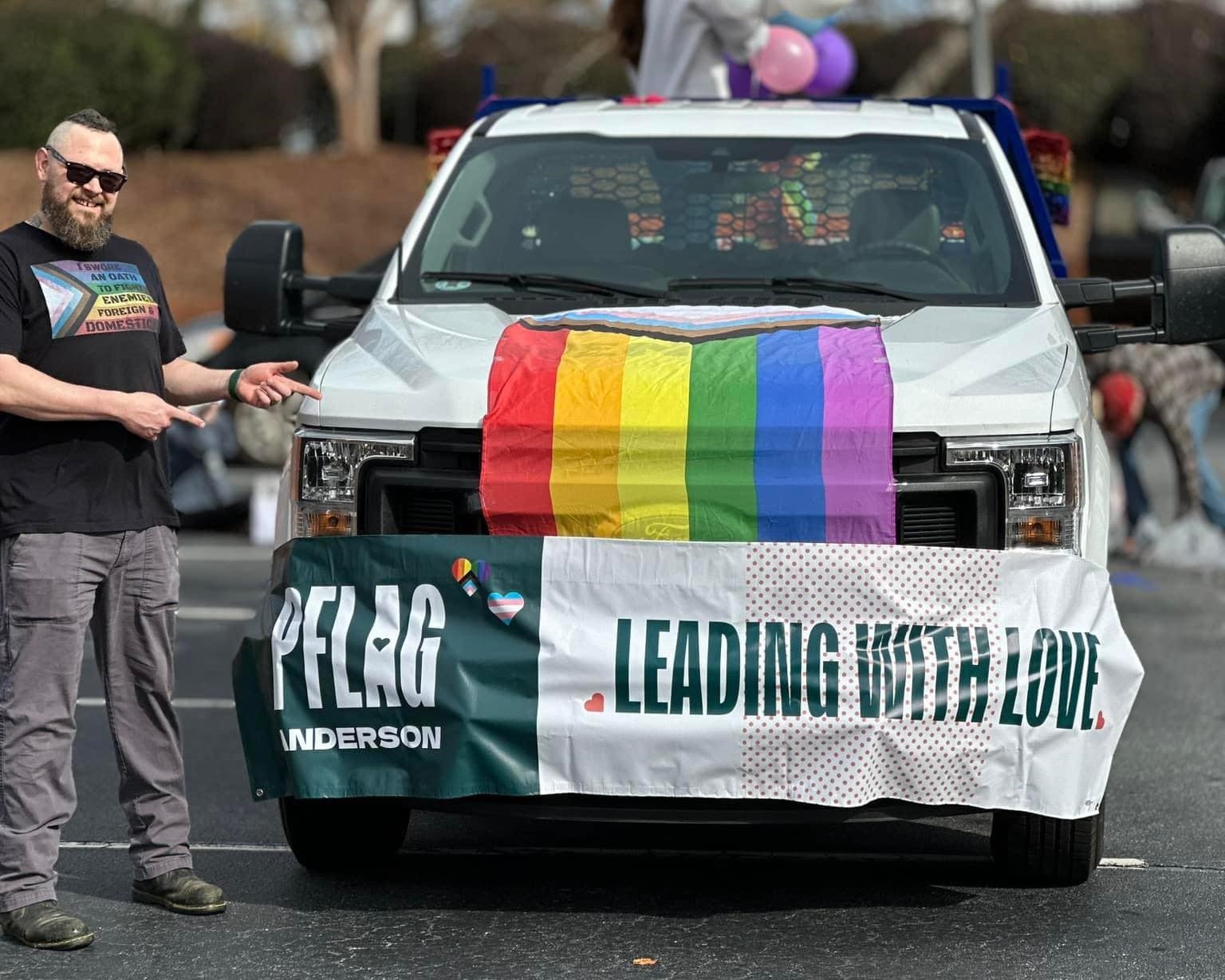 Eric standing beside a pickup truck preparing for a Pride parade. The truck has a rainbow flag and a PFLAG Anderson banner on the front with the slogan