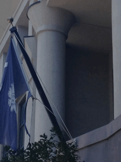 A tattered South Carolina flag hangs from a flagpole in front of the Charleston County School District office