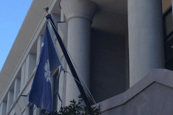 A tattered South Carolina flag hangs from a flagpole in front of the Charleston County School District office