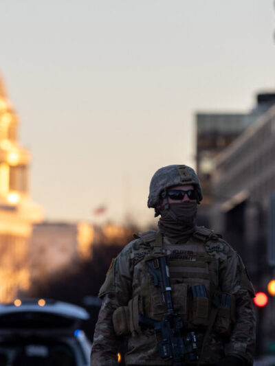 Photo of military personnel in tactical gear beside an armored vehicle in the street near a capital building