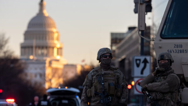 Photo of military personnel in tactical gear beside an armored vehicle in the street near a capital building