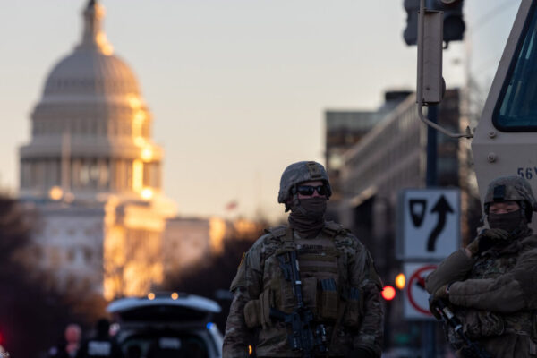 Photo of military personnel in tactical gear beside an armored vehicle in the street near a capital building