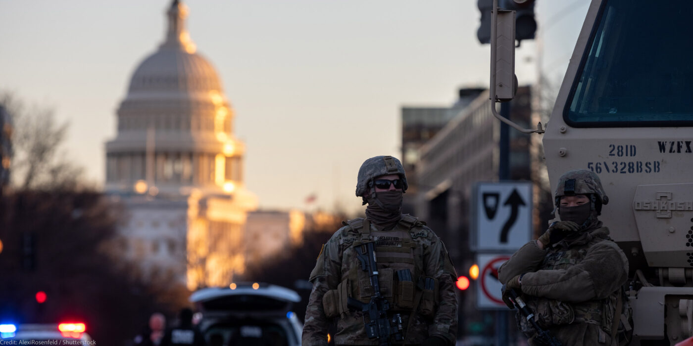 Photo of military personnel in tactical gear beside an armored vehicle in the street near a capital building