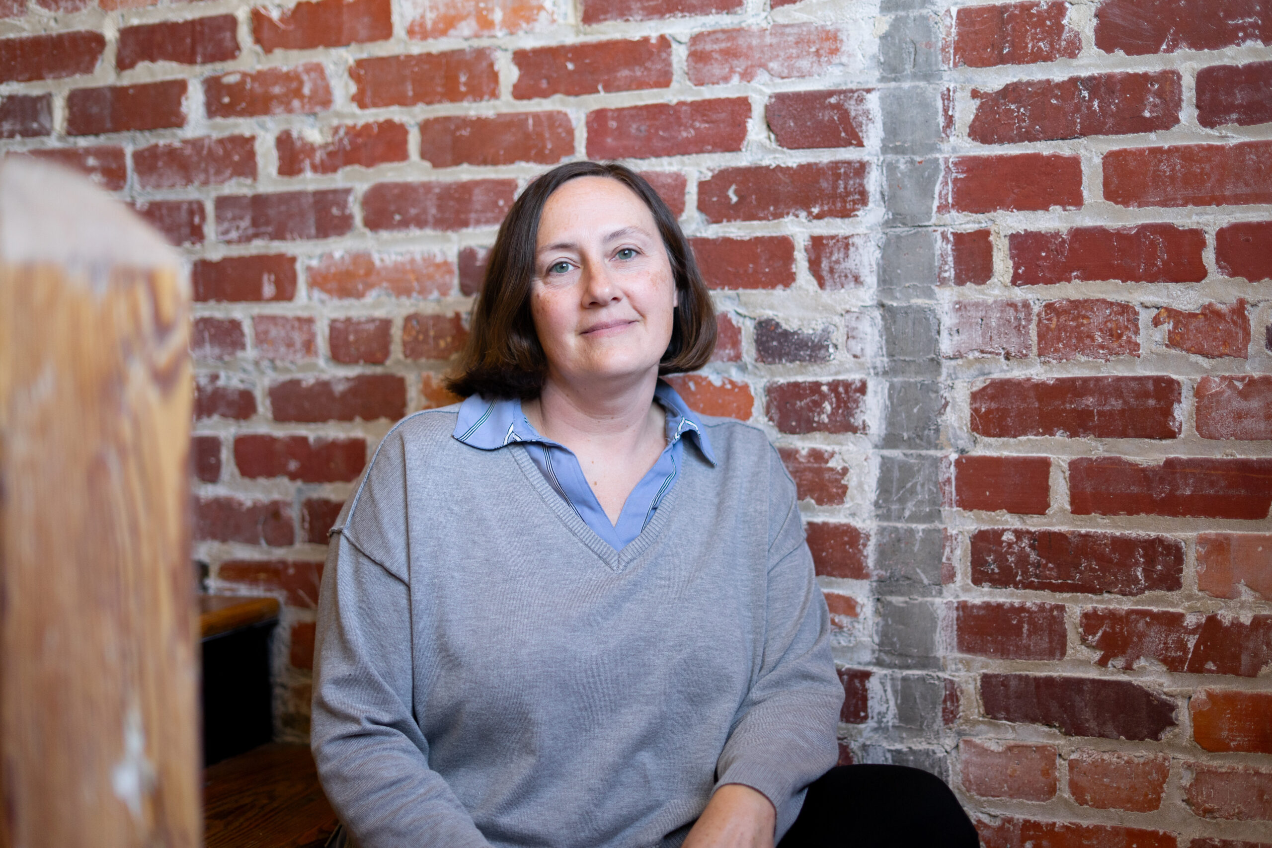 Photo of Dr. Emily Taylor a white woman with short hair in a gray sweater and collared shirt, in front of a weathered brick wall with natural light