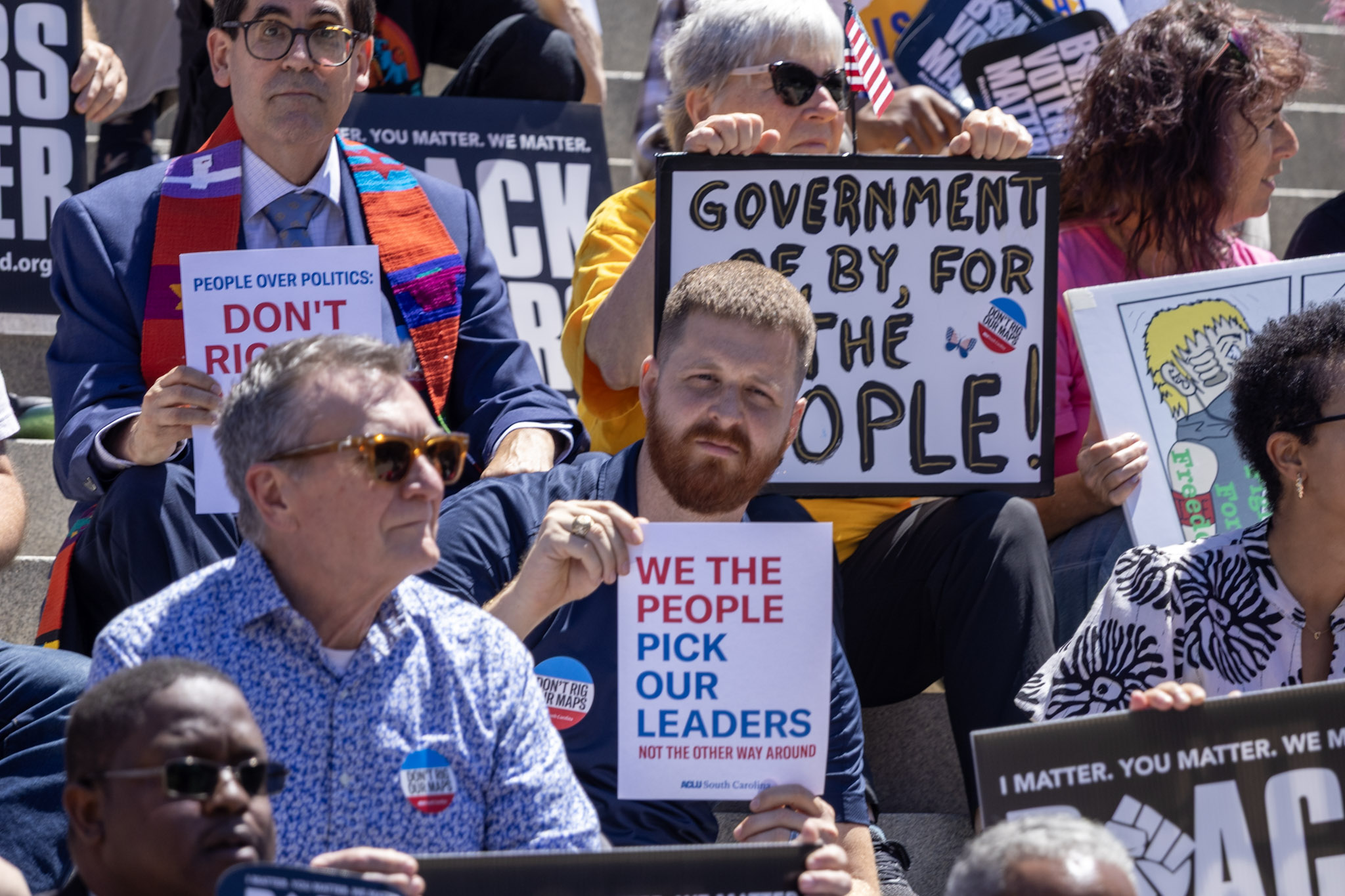A man in a crowd of protesters holds a sign that says "We the people pick our leaders, not the other way around"