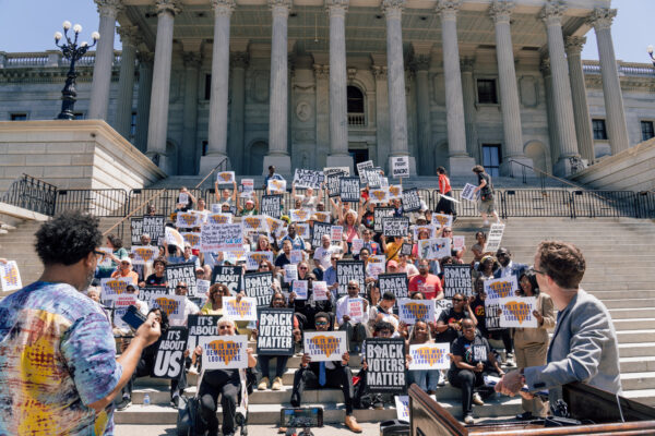 A crowd of protesters on the Statehouse steps. Signs say "This is what democracy looks like" and "Black voters matter."