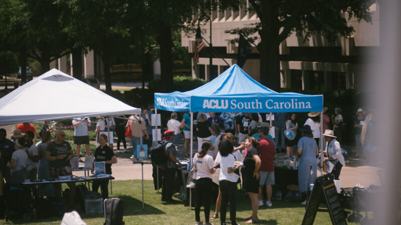 Protesters gather on the Statehouse lawn near an ACLU of South Carolina pop-up tent
