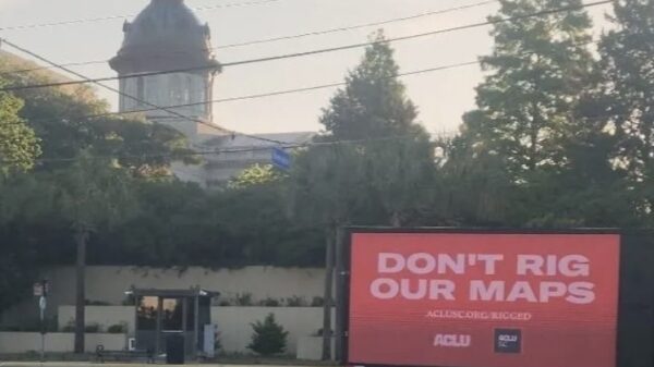 A billboard truck drives past the South Carolina Statehouse. A sign on the truck says "Don't rig our maps. aclusc.org/rigged"