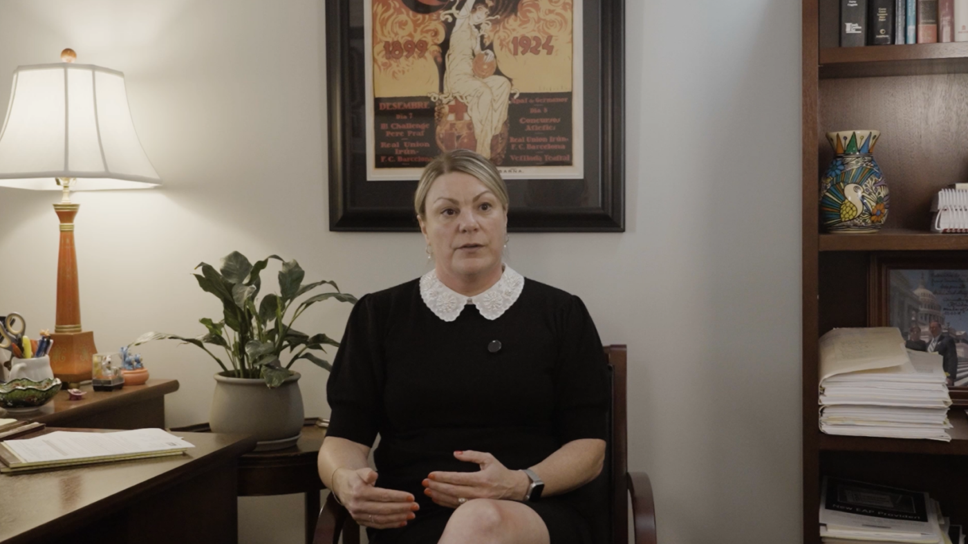 Image of white woman in black dress sitting in a chair with framed art behind her.