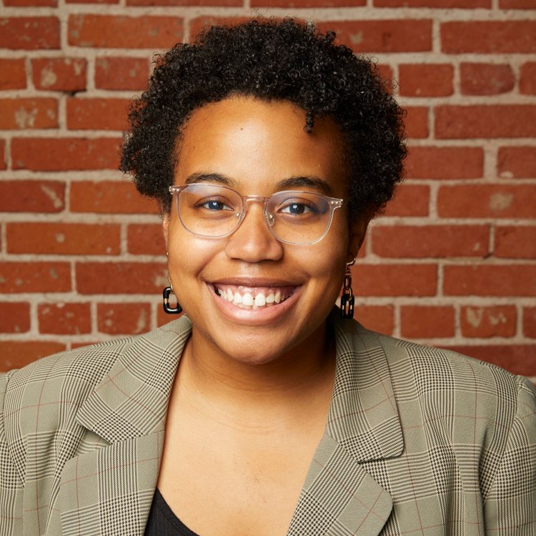 Professional headshot of Alexis Lefft, who is smiling while wearing glasses and a plaid blazer