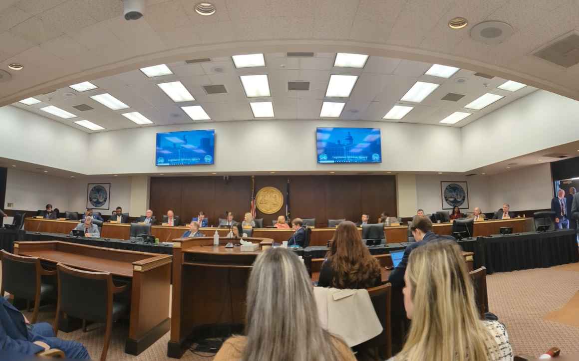 A panoramic shot of a committee of lawmakers under fluorescent lights in a conference room