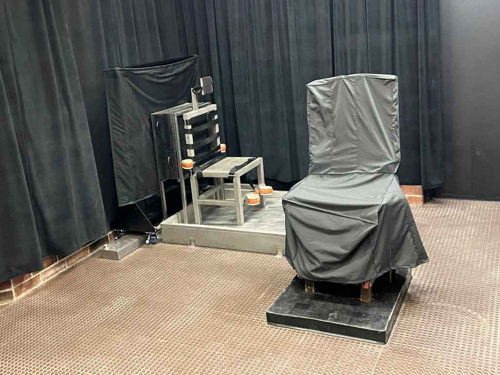 South Carolina's death chamber. A chair in the front is covered in gray cloth. Another chair is metal and has straps attached. The walls are covered by black curtains.