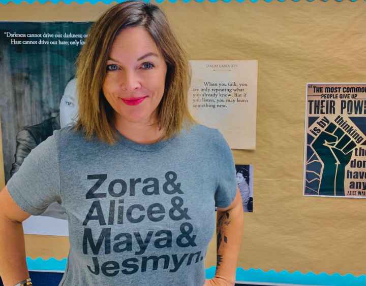 A photo of Mary Wood. She has shoulder-length brown hair and is wearing a gray T-shirt with the names "Zora & Alice & Maya & Jesmyn" on it.