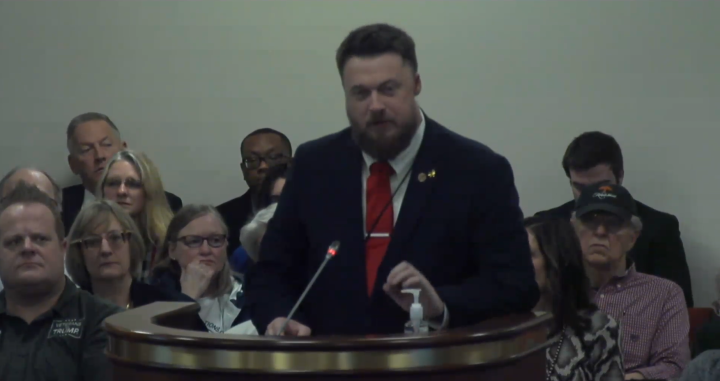 ACLU-SC Advocacy Strategist Matthew Butler addresses a subcommittee. He is wearing a suit and red tie and is standing behind a lectern with a microphone.