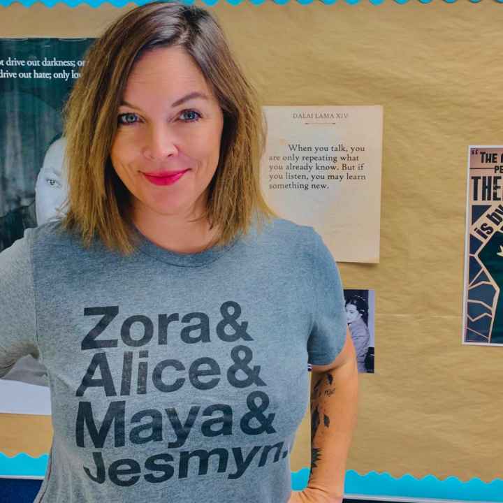 A photo of Mary Wood. She has shoulder-length brown hair and is wearing a gray T-shirt with the names "Zora & Alice & Maya & Jesmyn" on it.