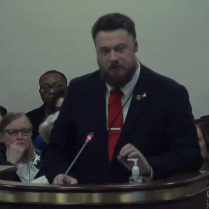 ACLU-SC Advocacy Strategist Matthew Butler addresses a subcommittee. He is wearing a suit and red tie and is standing behind a lectern with a microphone.