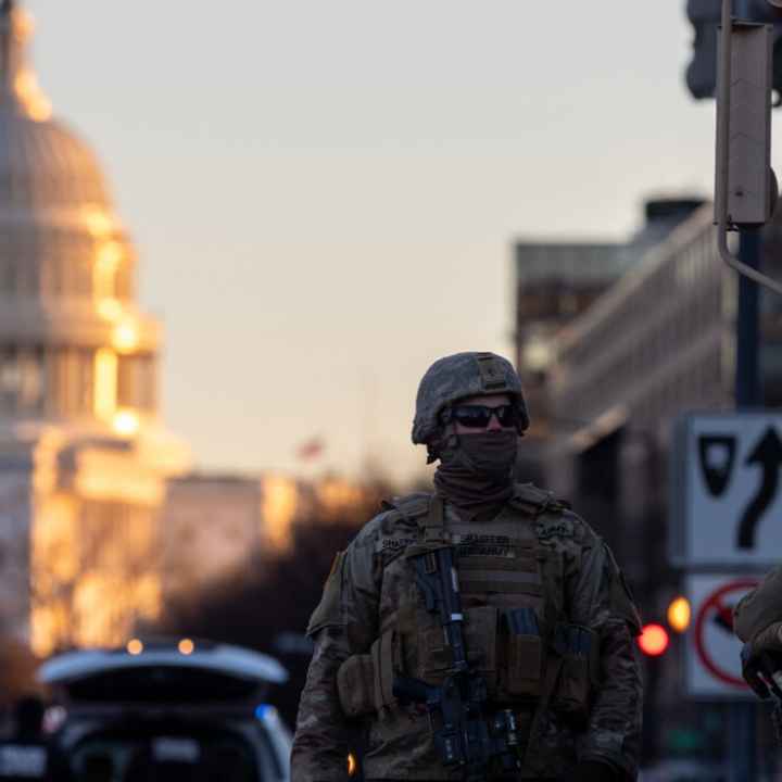Photo of military personnel in tactical gear beside an armored vehicle in the street near a capital building